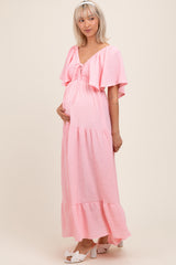 woman wearing a pink maternity maxi dress with frill sleeves and a tiered skirt, highlighting her baby bump