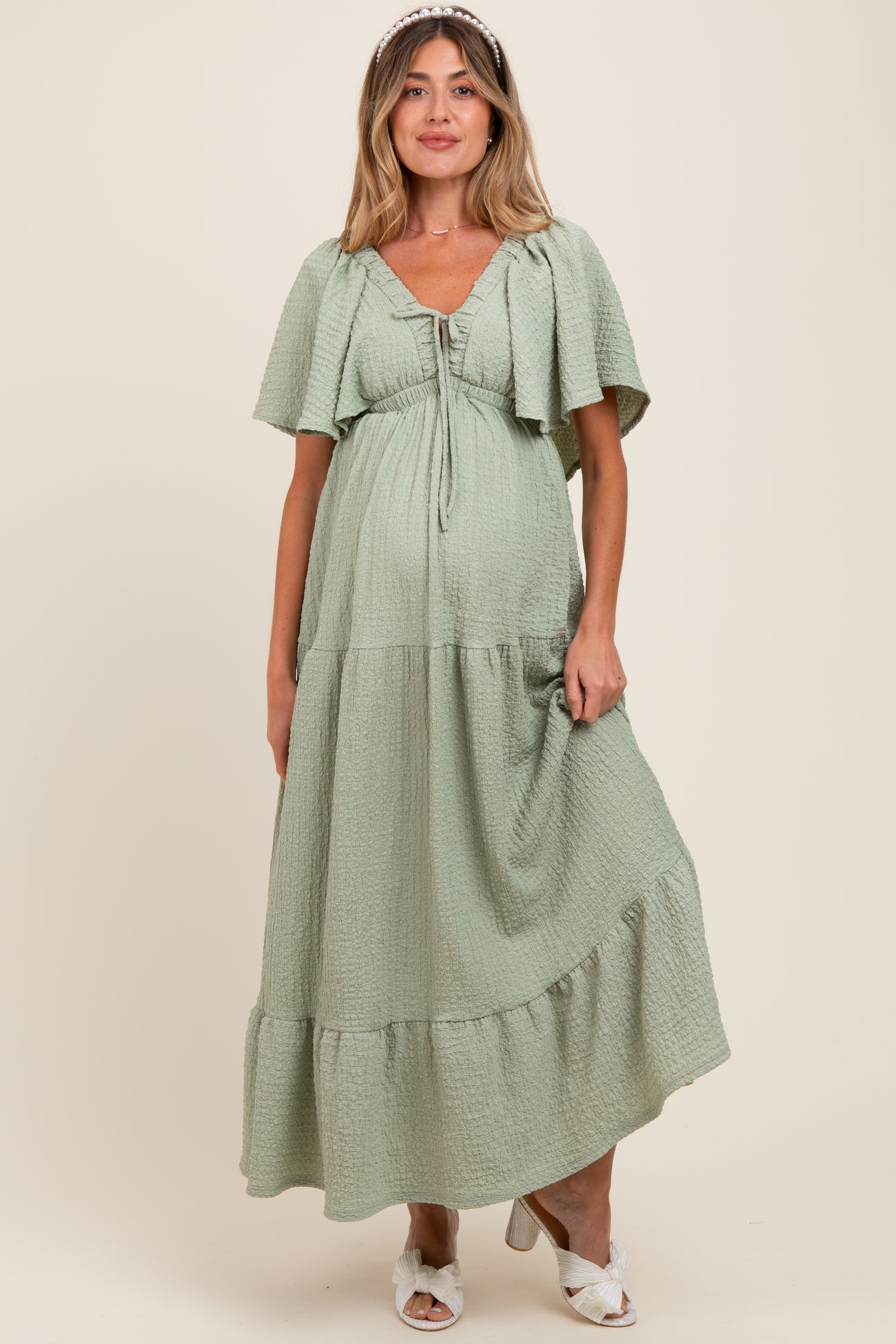 woman wearing a light green maternity maxi dress with flutter sleeves and a tiered hem, showing her baby bump