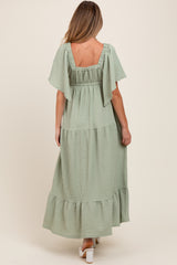 woman wearing a sage green maternity maxi dress with flutter sleeves and a tiered skirt
