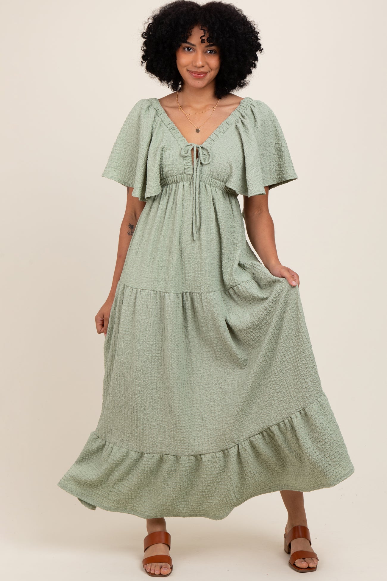 woman wearing a sage green tiered maxi dress with flutter sleeves and a tie front detail