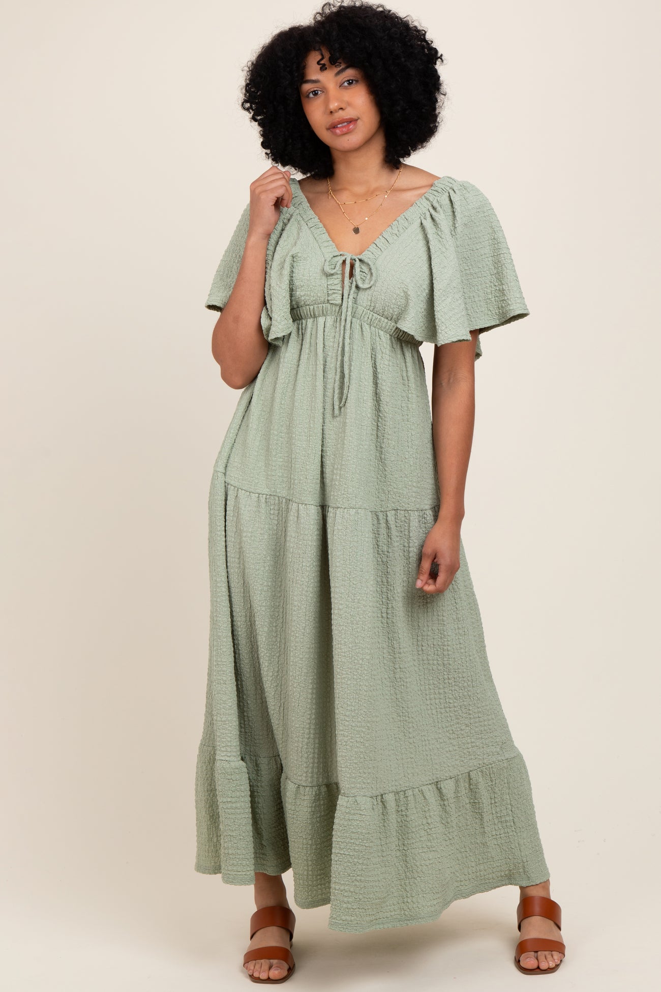 woman wearing a light green tiered maxi dress with short sleeves and tie detail at the neckline