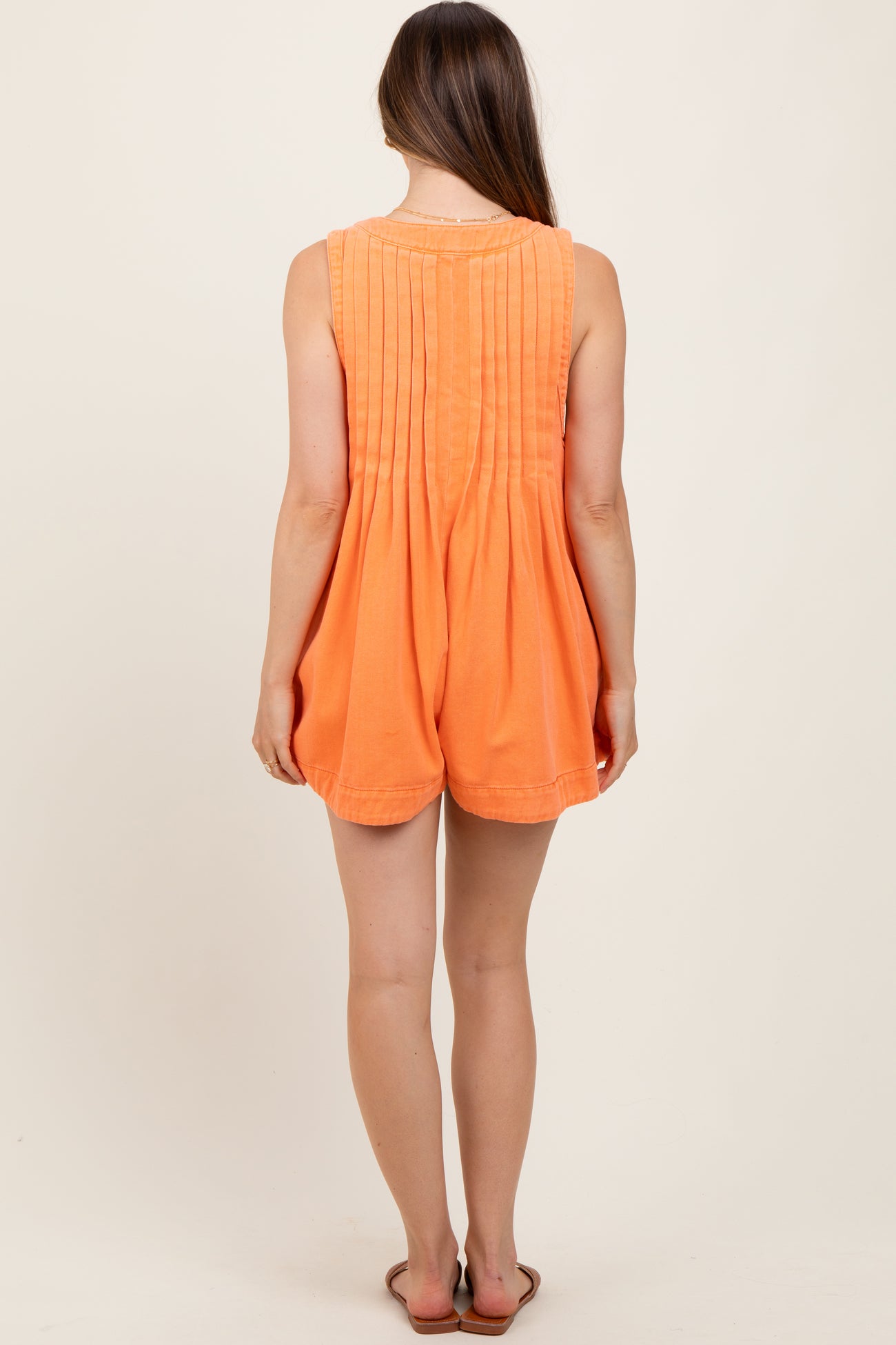 woman wearing an orange maternity romper with pleated back detail, showing a casual summer style