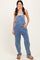 woman wearing light blue denim overalls with a fitted top and casual sandals, standing with hands in pockets