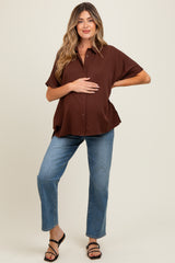 woman wearing a brown oversized maternity shirt and light blue jeans, holding her baby bump