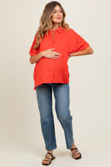 woman wearing a bright red short sleeve maternity blouse and holding her baby bump, paired with blue jeans