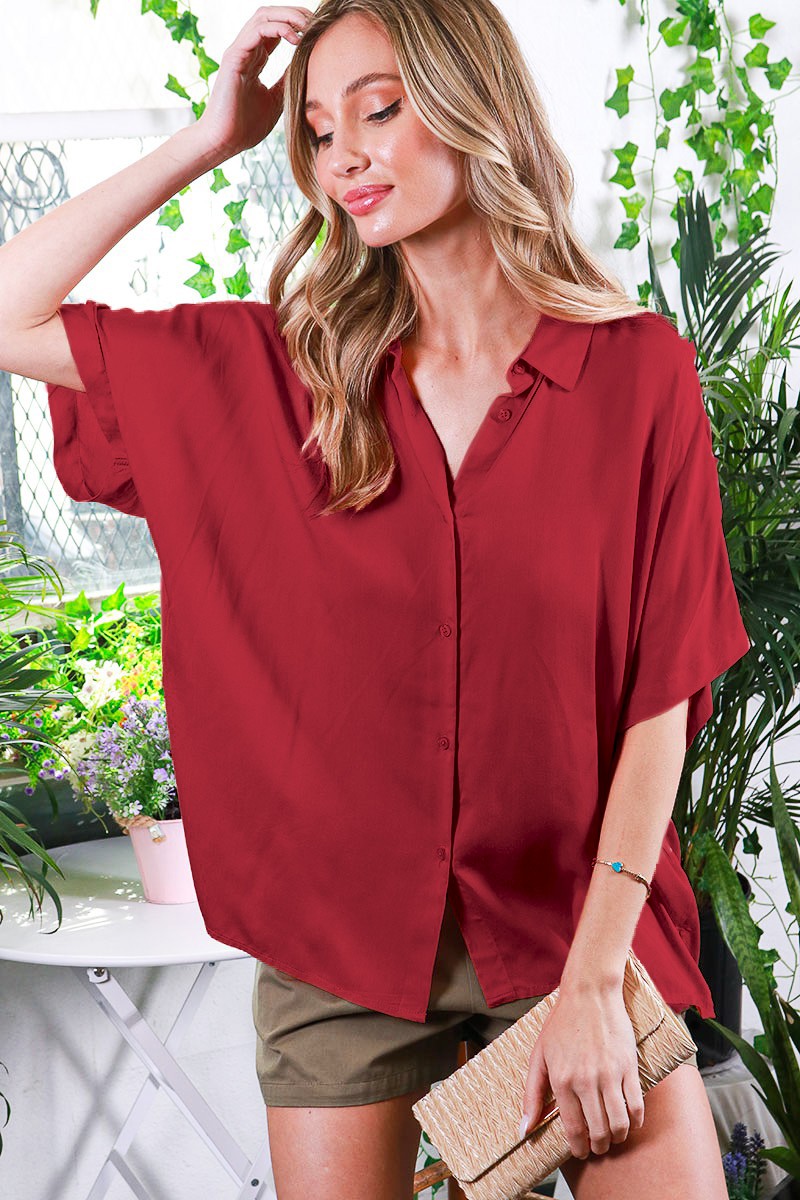 woman wearing a burgundy oversized button-up shirt with short sleeves and styled with khaki shorts and a clutch purse