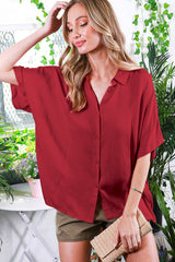 woman wearing a burgundy oversized button-up shirt with short sleeves and styled with khaki shorts and a clutch purse