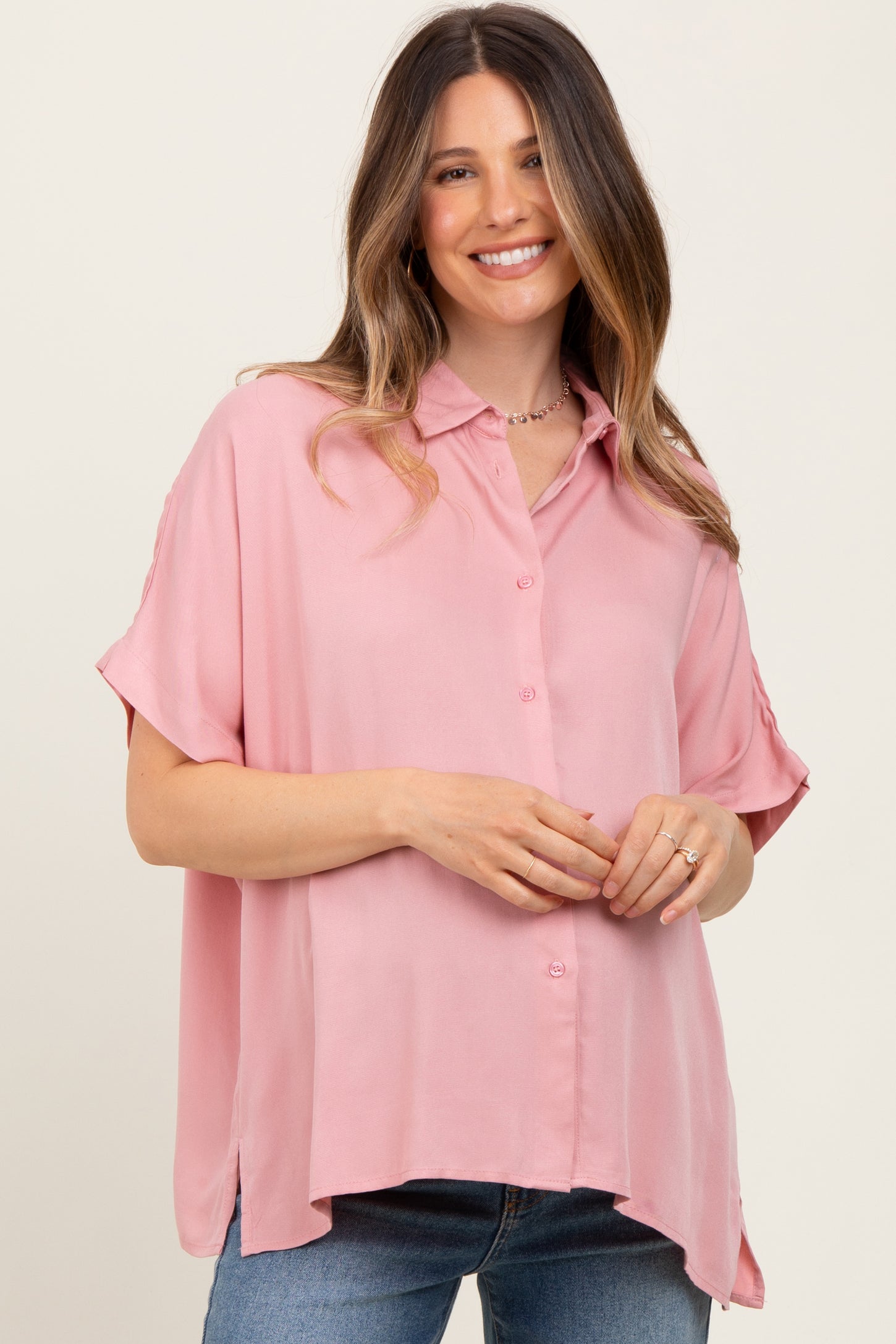 woman wearing a light pink short sleeve button-up maternity top with a relaxed fit and a visible baby bump