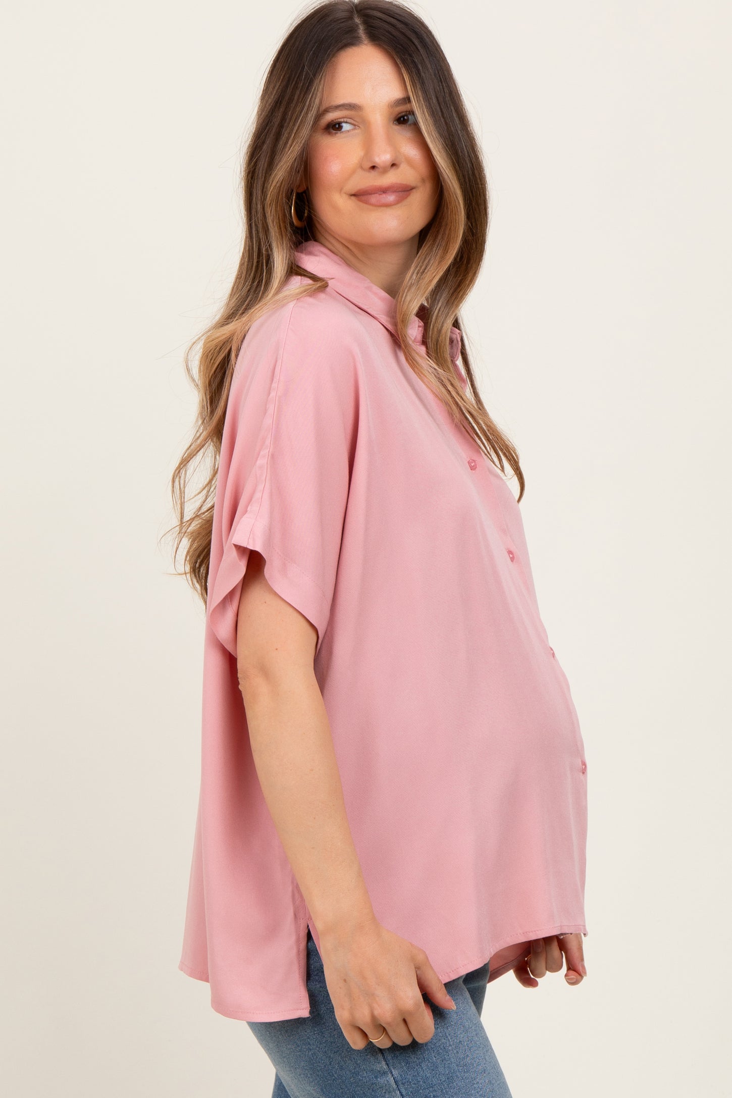 woman wearing a light pink maternity button-up shirt and showing her baby bump