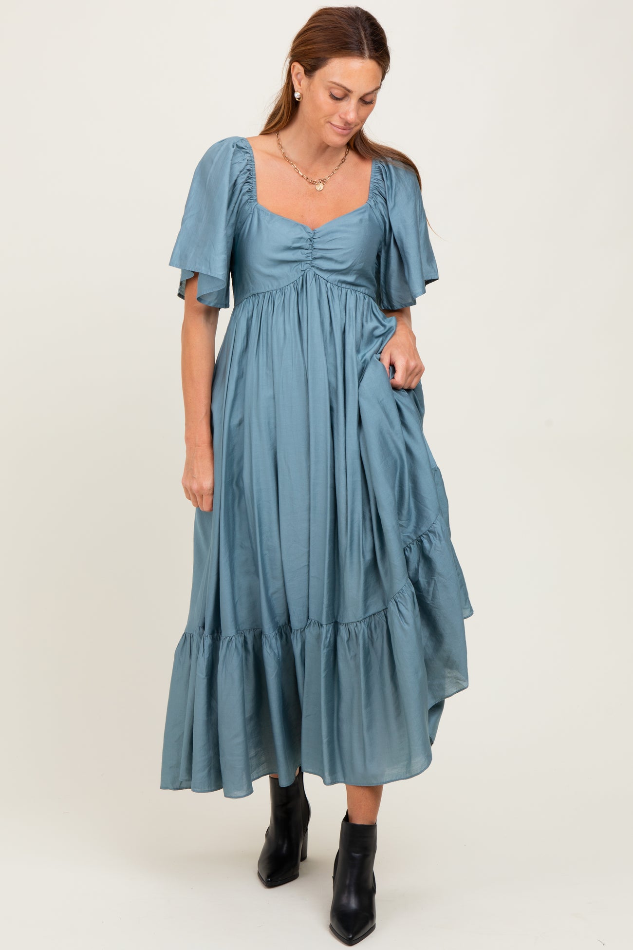 woman wearing a teal puff sleeve midi dress with a square neckline and ruffled hemline, paired with black ankle boots
