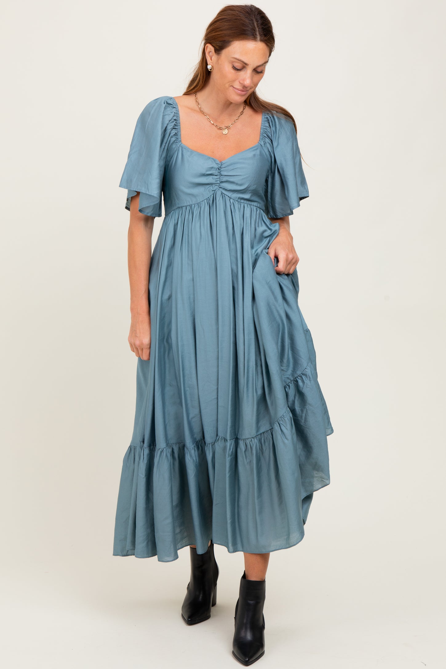 woman wearing a teal puff sleeve midi dress with a square neckline and ruffled hemline, paired with black ankle boots