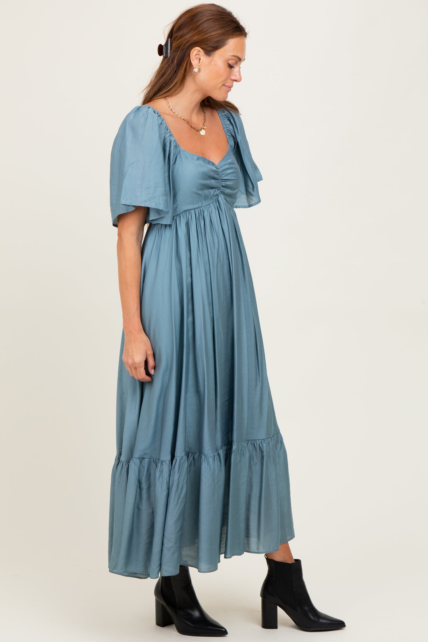 woman wearing a teal shoulder-baring maxi dress with puff sleeves and a gathered bodice, paired with black ankle boots