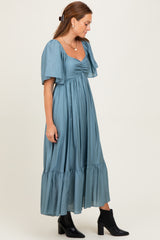 woman wearing a teal shoulder-baring maxi dress with puff sleeves and a gathered bodice, paired with black ankle boots