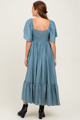 woman wearing a back view of a blue maxi dress with puff sleeves and a smocked bodice