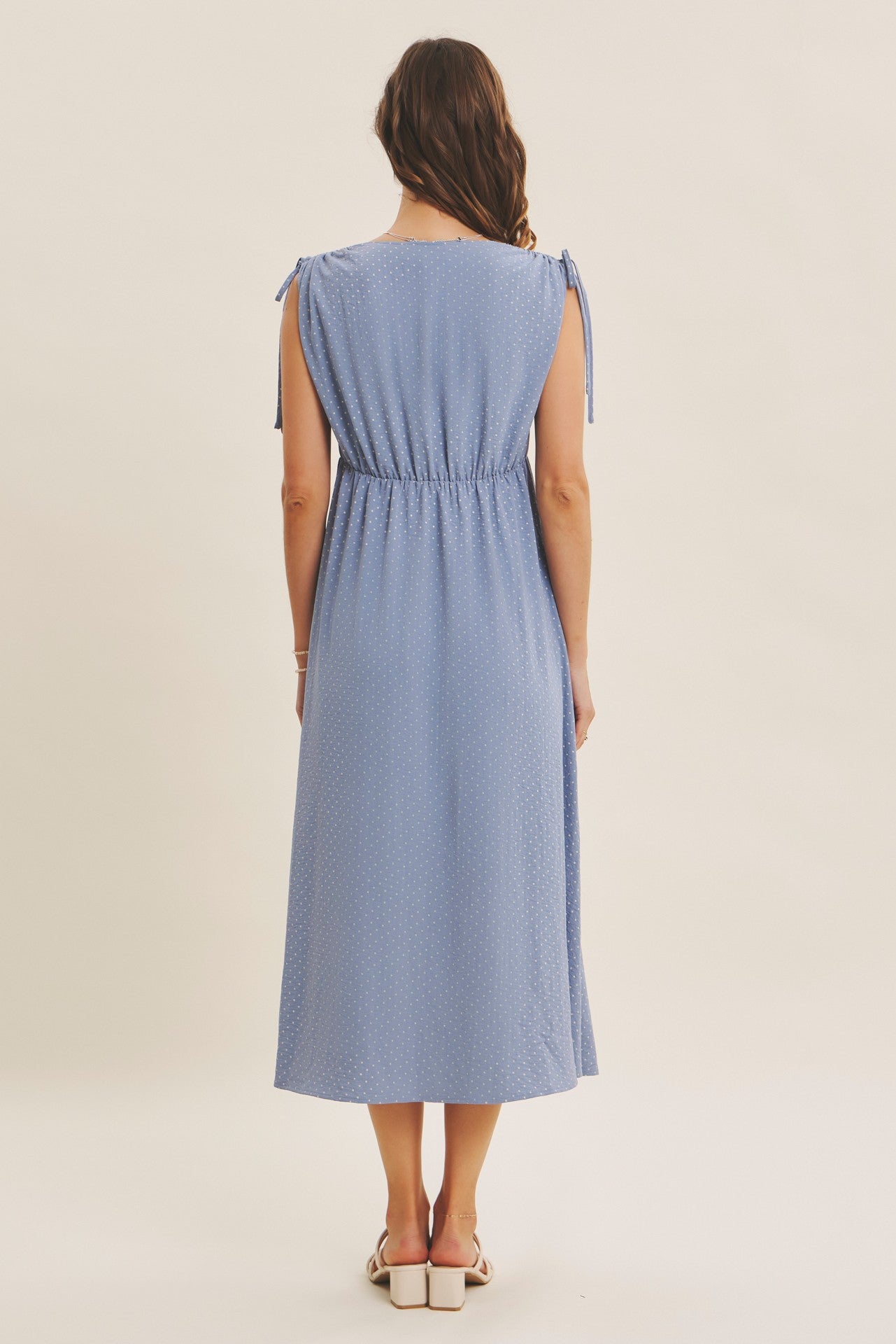 woman wearing a light blue midi dress with tie sleeves and a gathered waist, viewed from the back