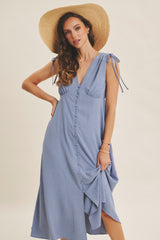 woman wearing a light blue polka dot midi dress with tie straps and a front slit, accessorized with a wide-brimmed straw hat