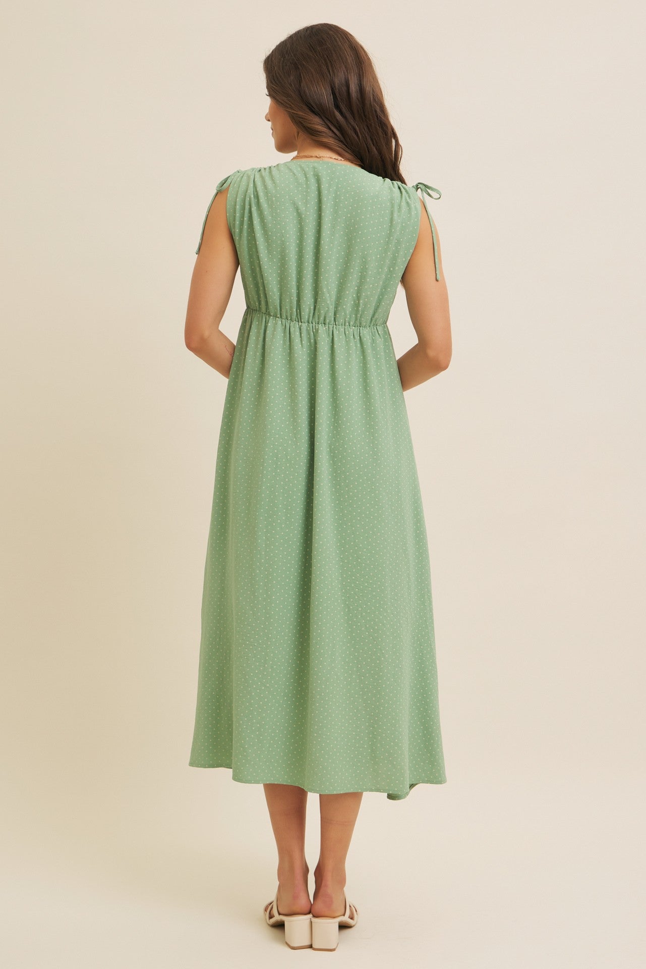 woman wearing a green midi dress with short sleeves and tie details at the shoulders, viewed from the back