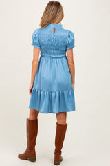 woman wearing a light blue maternity dress with smocked bodice and ruffled hem, standing with back to the camera