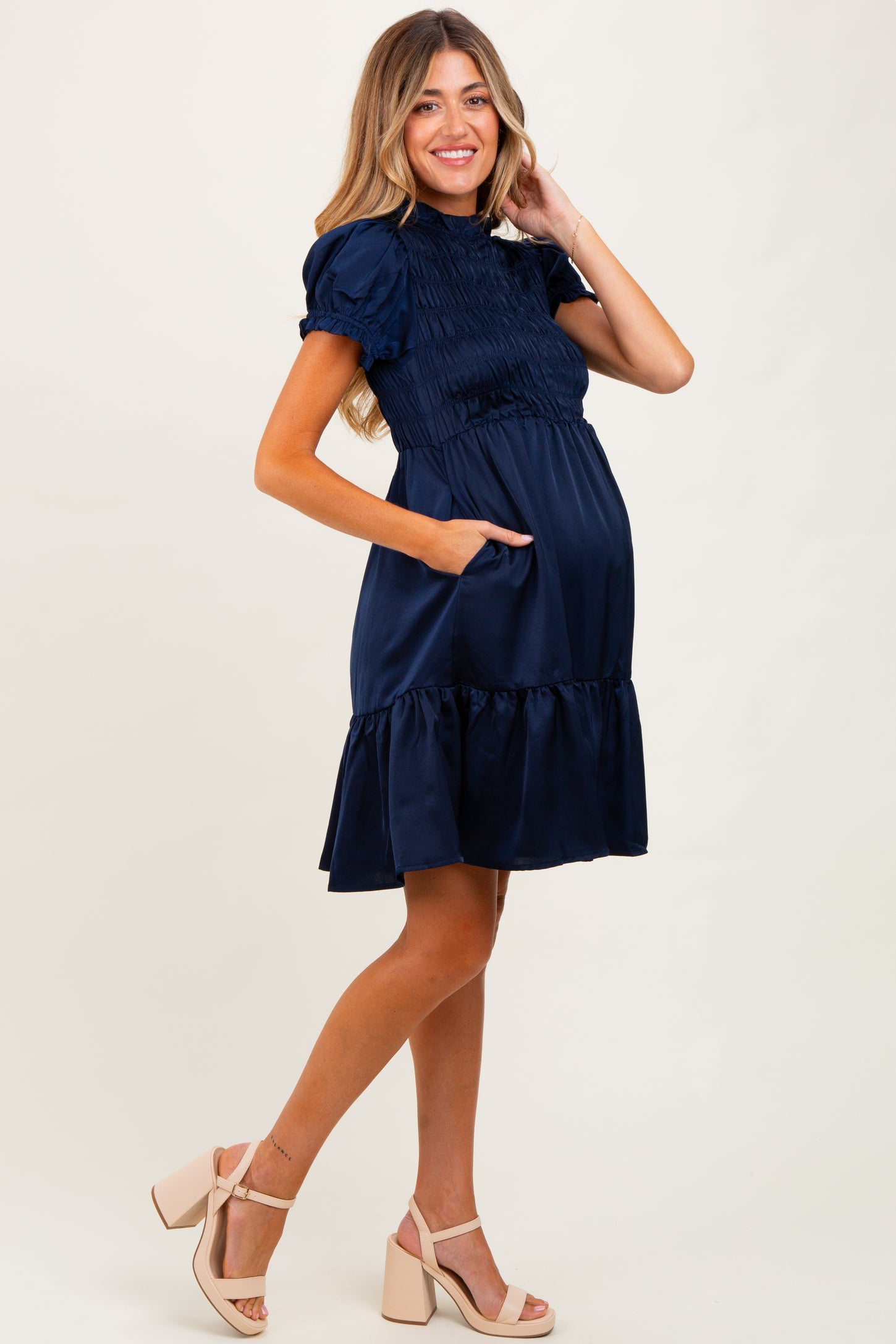 woman wearing a navy blue short sleeve maternity dress with smocked bodice and ruffled hem, holding a baby bump