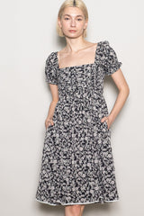 woman wearing a black floral puff sleeve dress with a square neckline and pockets