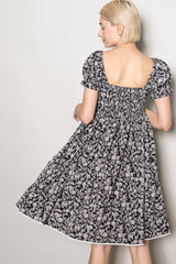 woman wearing a black floral print short sleeve dress with a square back and gathered waist