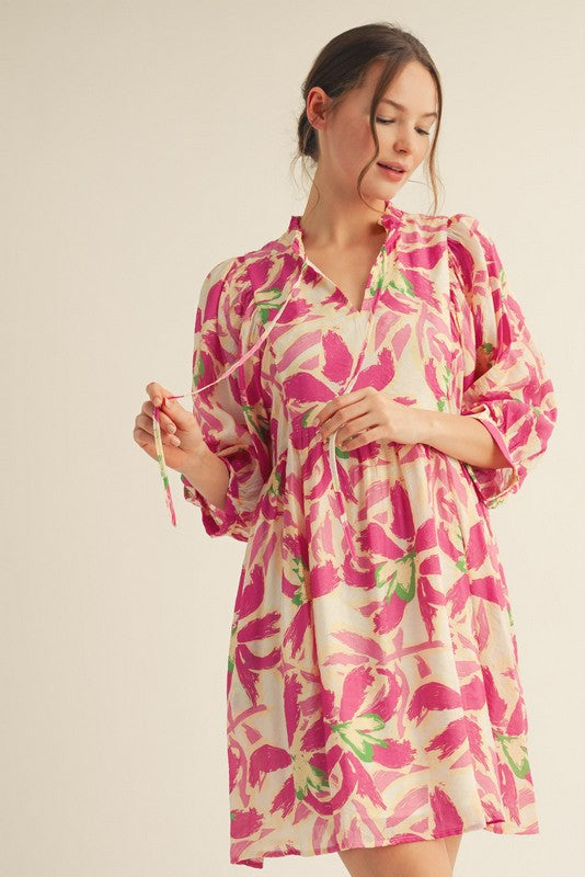 woman wearing a pink floral print short dress with puff sleeves and a relaxed fit, holding a string detail