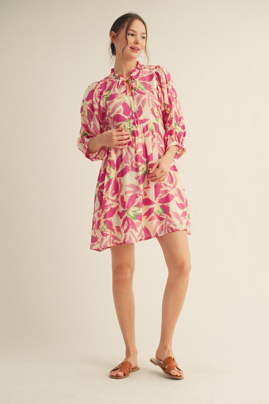 woman wearing a floral pink and green short dress with puff sleeves and a tie neckline