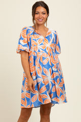 woman wearing a maternity short sleeve dress with a floral pattern in blue and orange, smiling and standing with hands on hips