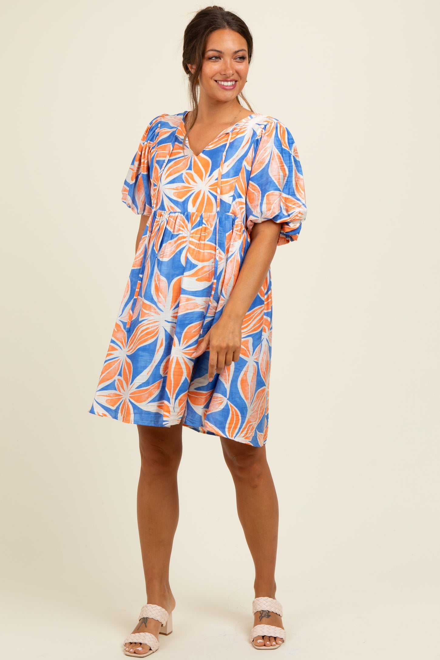 woman wearing a colorful floral print maternity dress with puffed sleeves and a loose fit, showcasing her baby bump