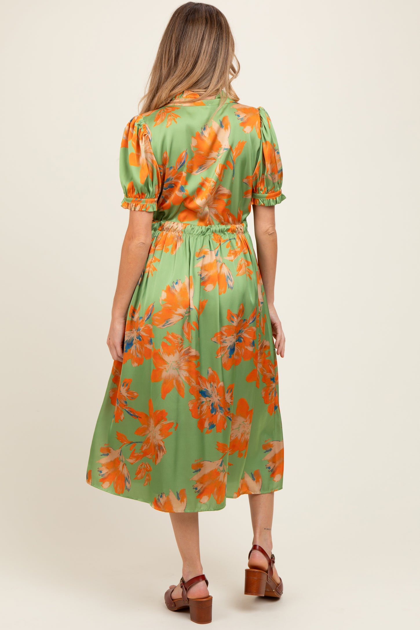 woman wearing a green floral midi maternity dress with puff sleeves and a cinched waist, showing her baby bump