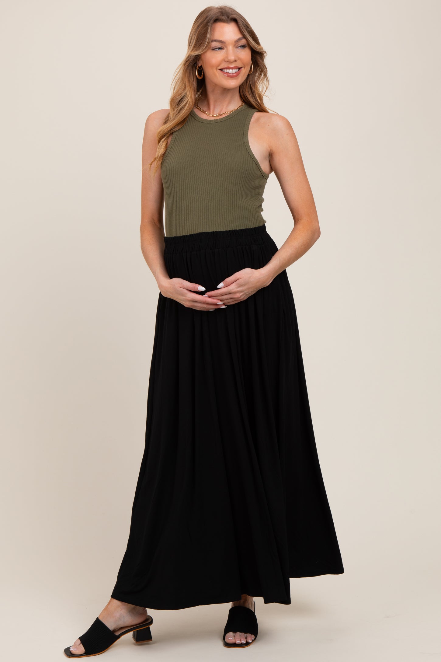 woman wearing a dark olive ribbed maternity tank top and a black maxi skirt, holding her baby bump