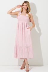 woman wearing a pink floral print maxi dress with smocked bodice and tie straps, featuring pockets and a tiered skirt