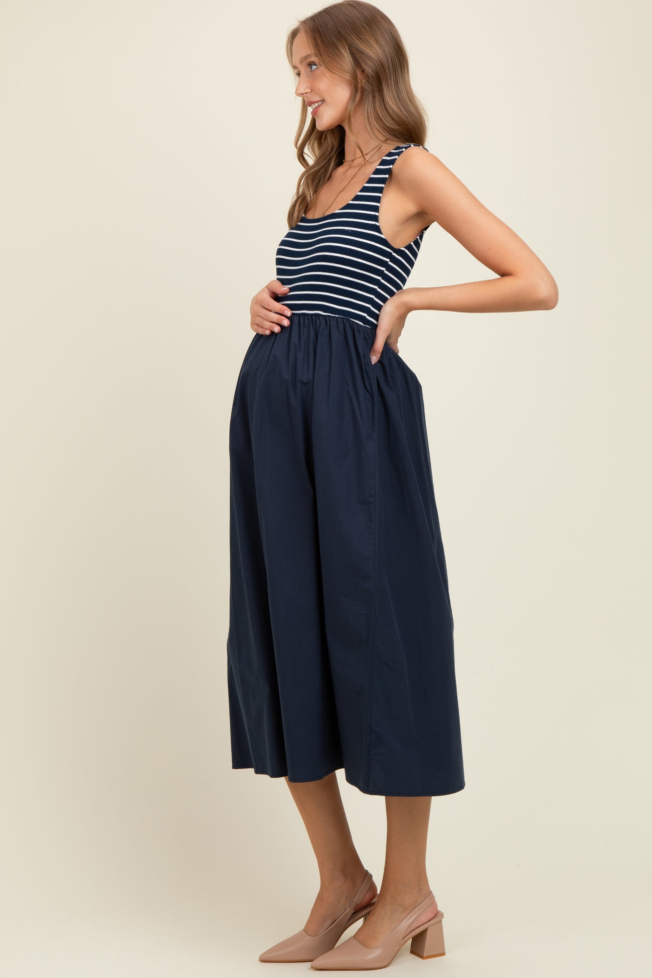 woman wearing a navy and white striped maternity dress with a fitted top and flowy skirt, holding her baby bump