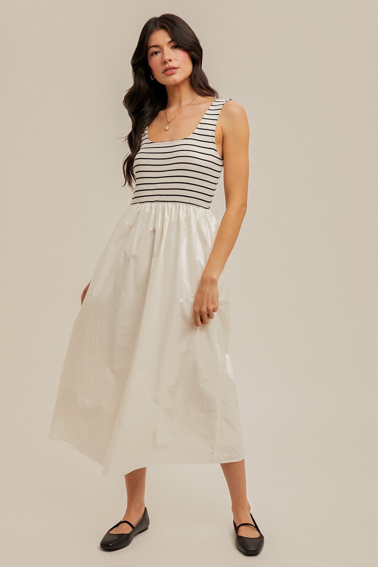 woman wearing a striped sleeveless midi dress with a fitted bodice and a flowing white skirt, paired with black flats