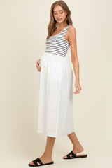 woman wearing a striped maternity tank top and a flowy white maternity midi skirt, gently holding her baby bump