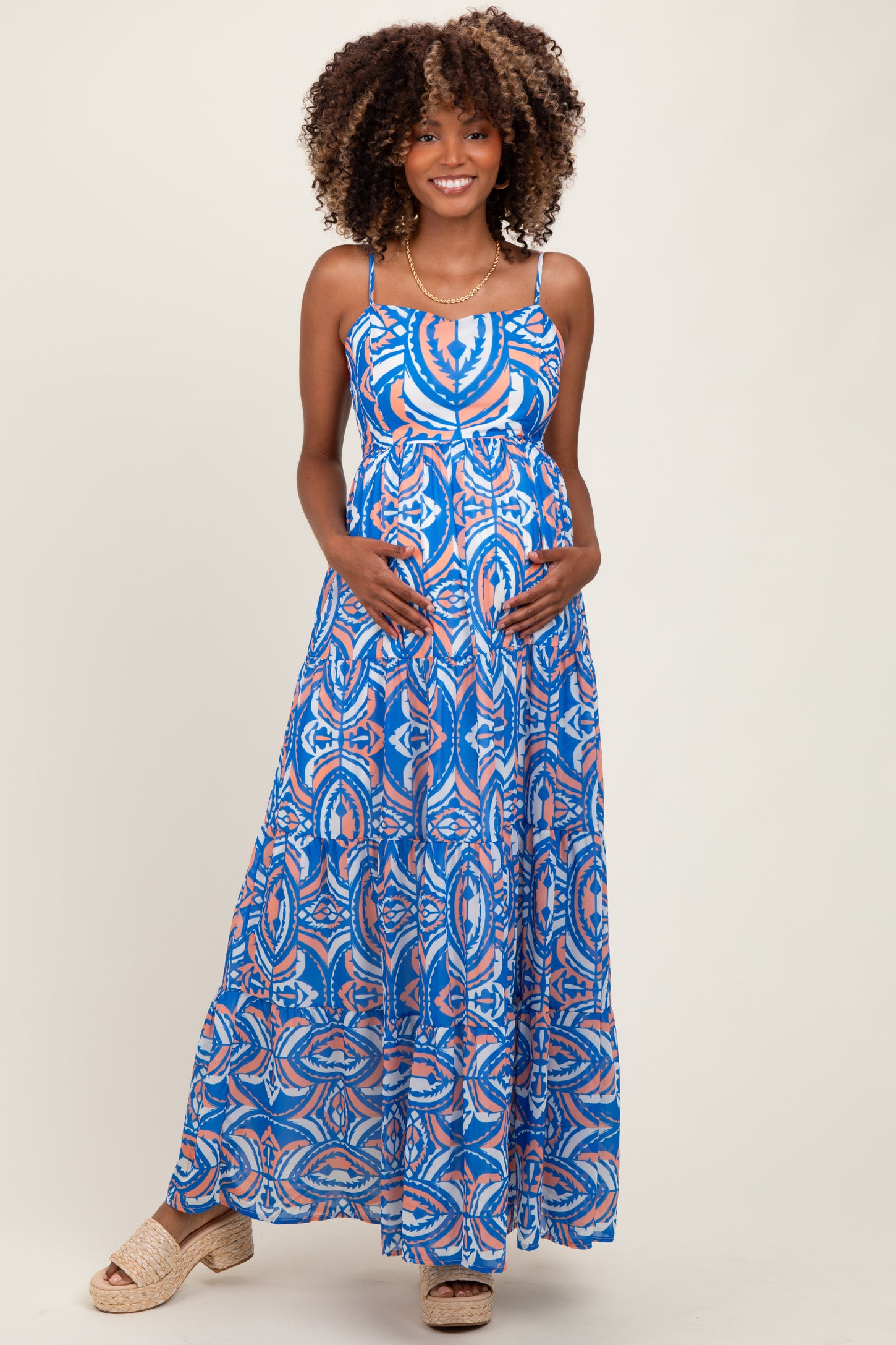woman wearing a blue patterned maternity maxi dress and holding her baby bump