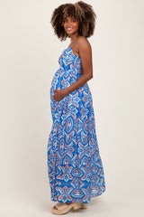 woman wearing a blue patterned maxi maternity dress and cradling her baby bump