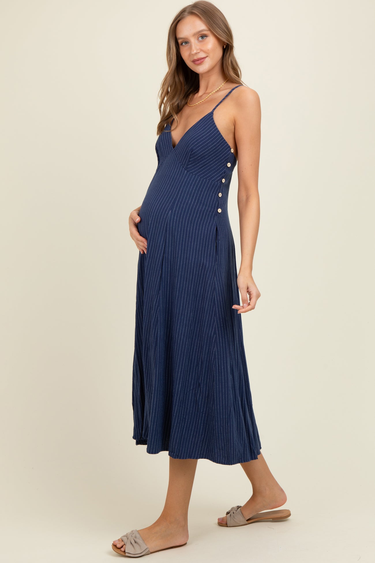 woman wearing a navy blue maternity dress with spaghetti straps and button detailing, showing her baby bump