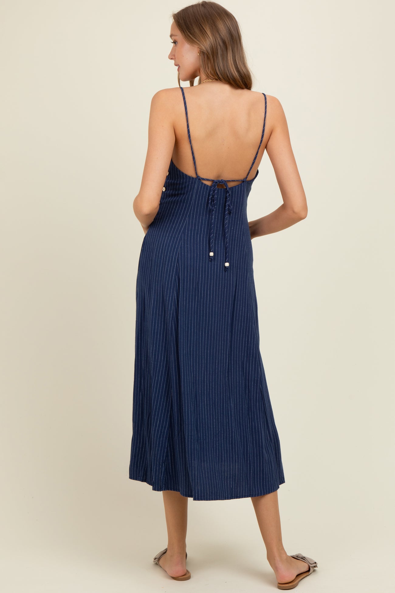 woman wearing a navy blue striped maternity dress with adjustable straps and a back tie detail