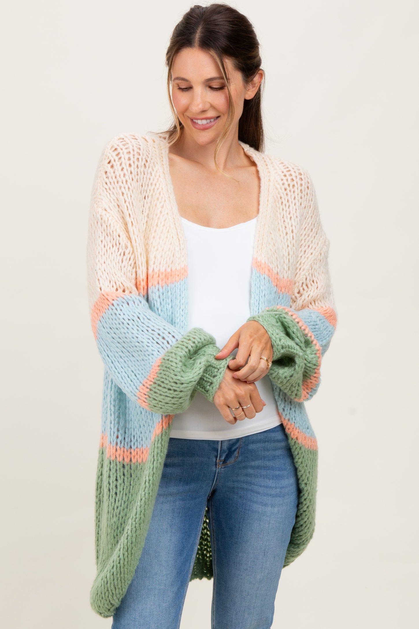 woman wearing a pastel colored open knit maternity cardigan over a white top with blue jeans and a relaxed smile