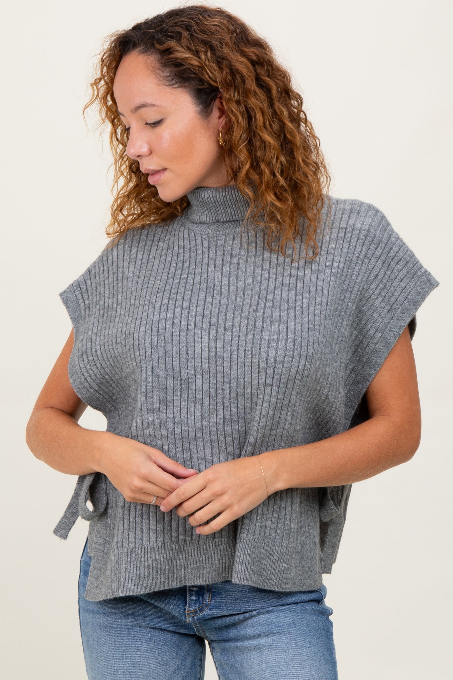 woman wearing a gray ribbed knit poncho with a mock turtleneck and side ties, paired with blue jeans