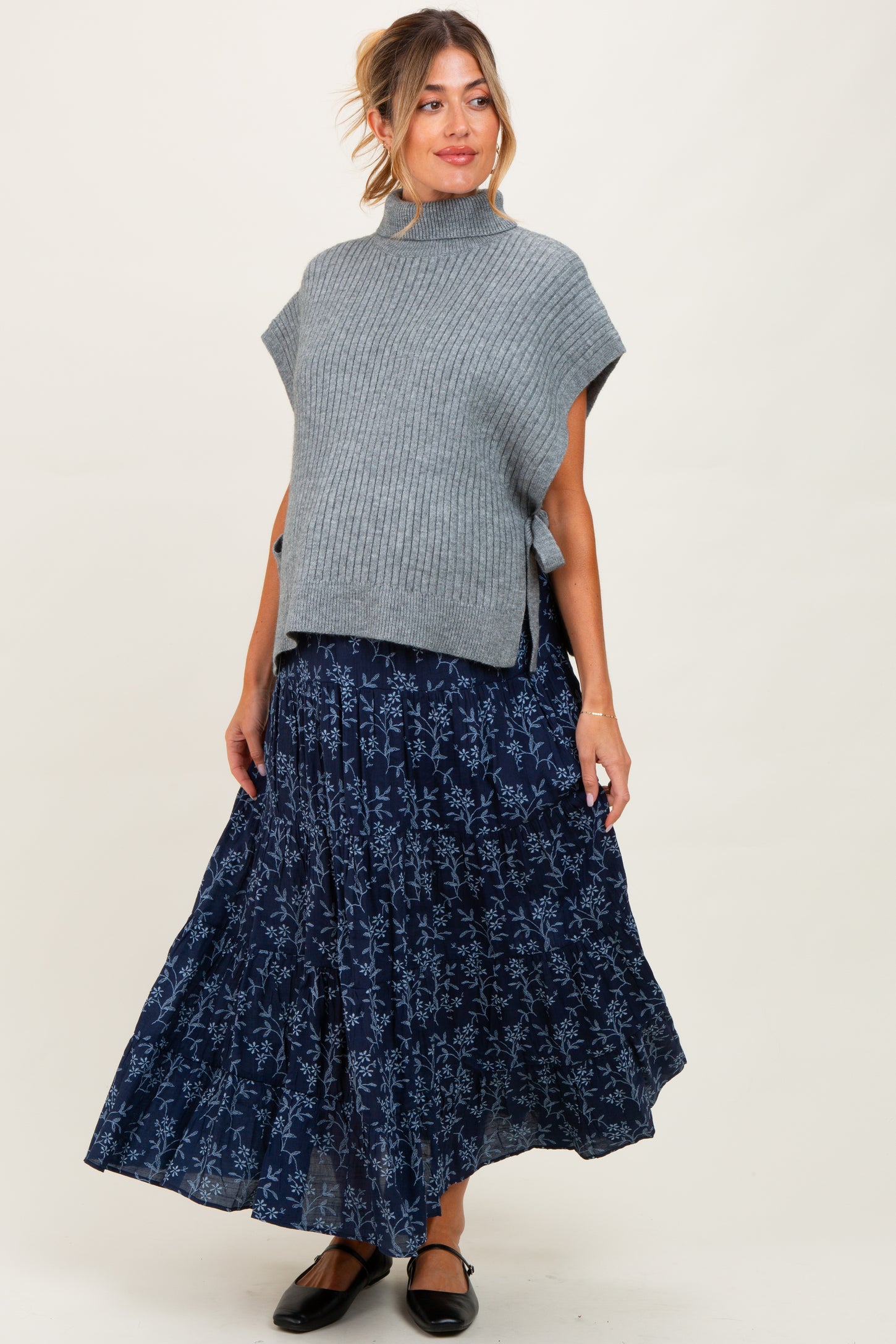woman wearing a gray oversized sweater and a flowy navy floral maternity skirt, showcasing her baby bump