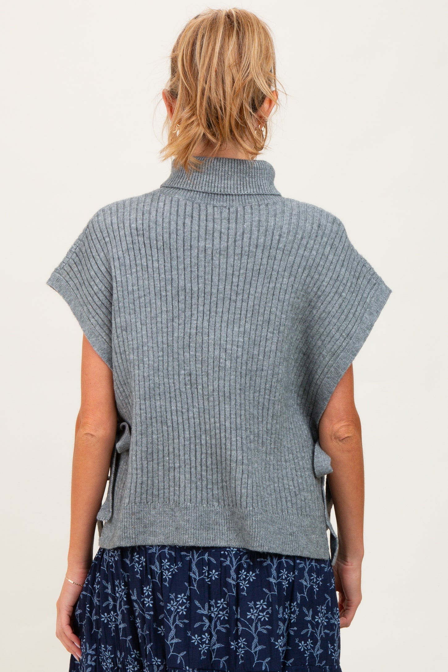 woman wearing a gray ribbed maternity sweater with short sleeves, styled over a floral skirt, showing a relaxed fit from the back
