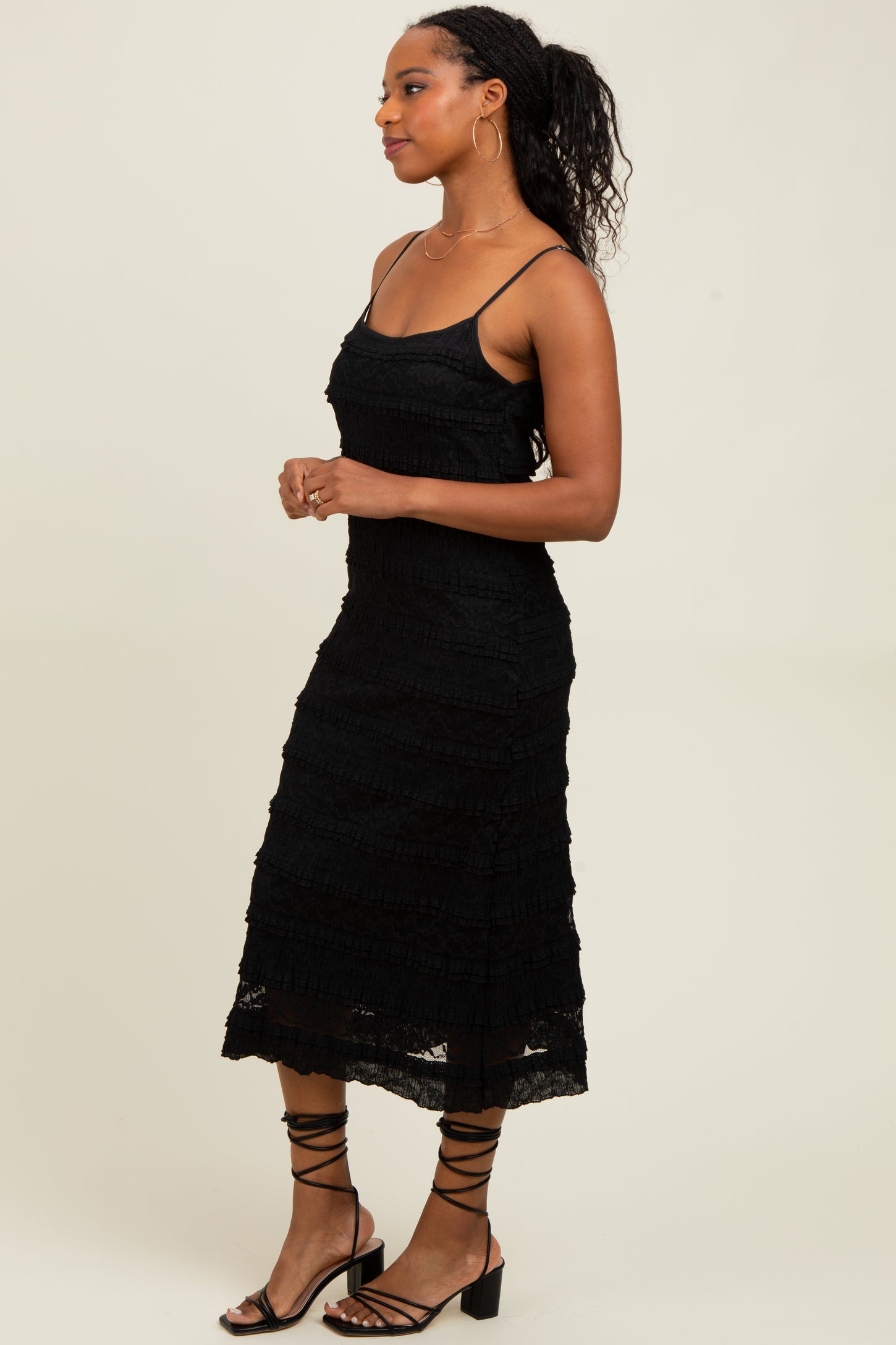 woman wearing a black sleeveless midi dress with a tiered design and strappy sandals
