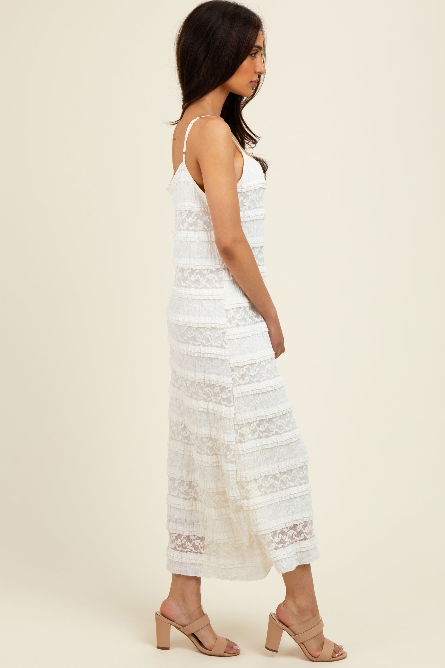 woman wearing a white lace maxi dress with adjustable straps and a tiered design, styled with beige block heel sandals