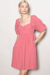woman wearing a pink short sleeve dress with a square neckline and puff sleeves, featuring side pockets