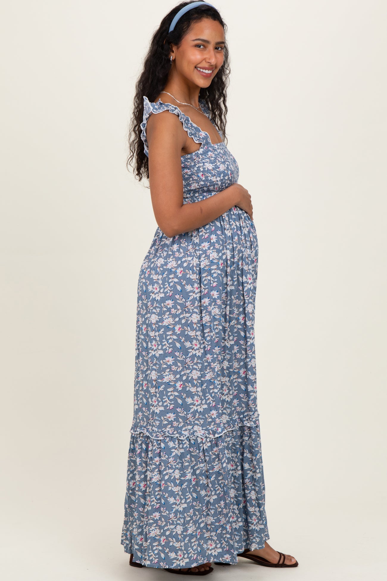 woman wearing a blue floral maternity maxi dress with ruffled straps and holding her baby bump