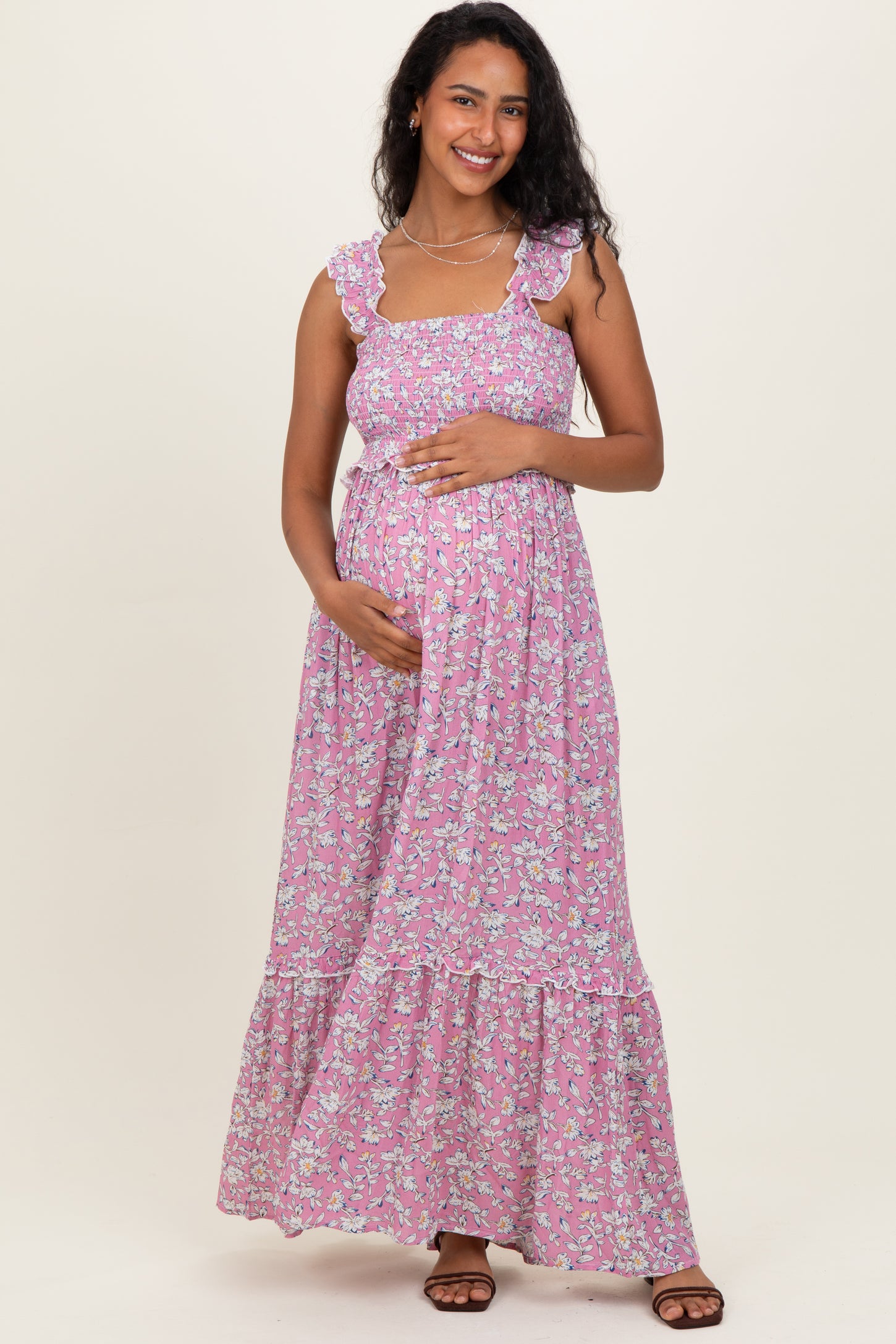 woman wearing a pink floral maternity maxi dress with ruffled straps and holding her baby bump