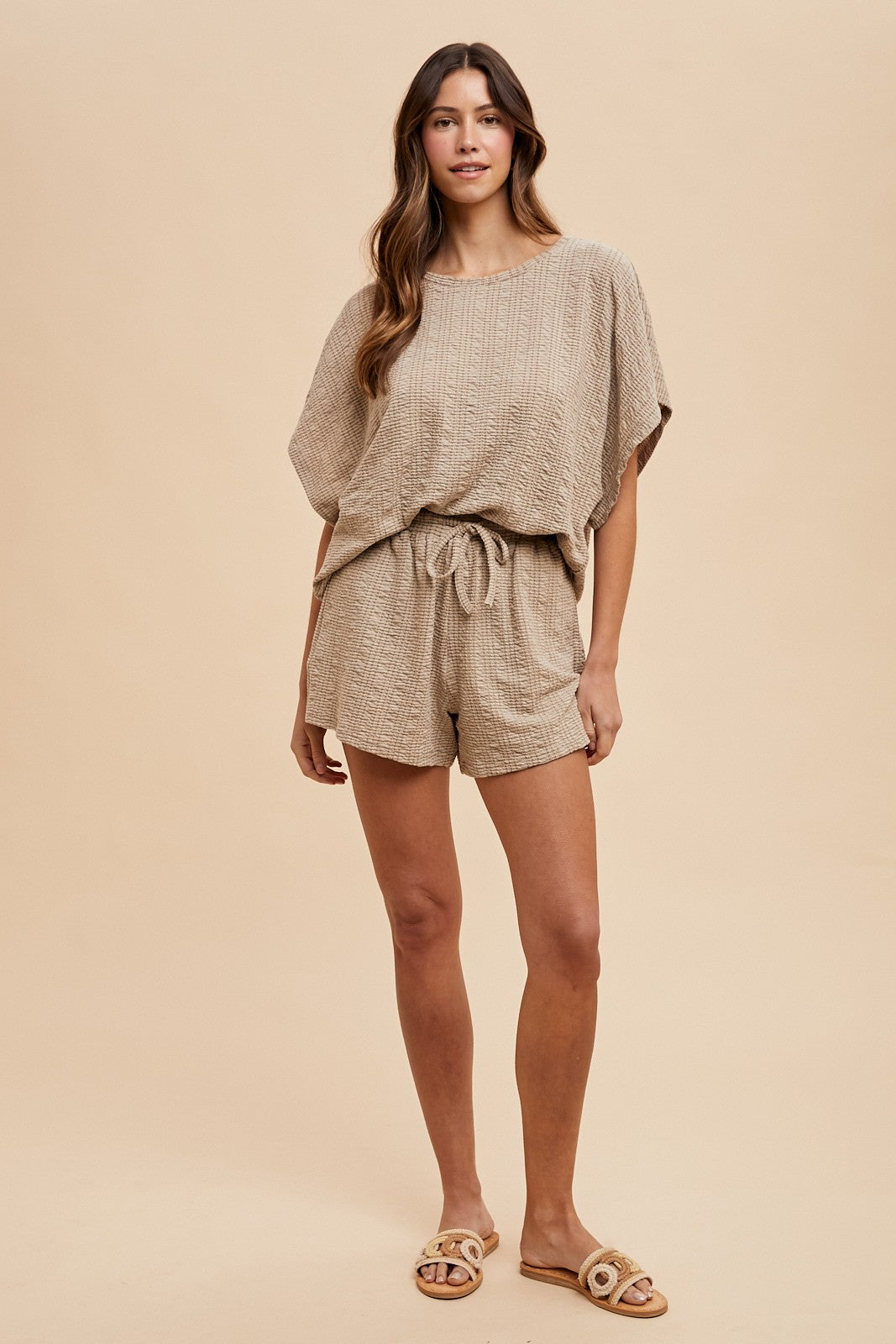 woman wearing a beige patterned knit short set with a drawstring waist and relaxed fit, styled with comfortable sandals