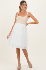 woman wearing a beige maternity dress with a fitted bodice and a white eyelet skirt, posing with one hand on her hip